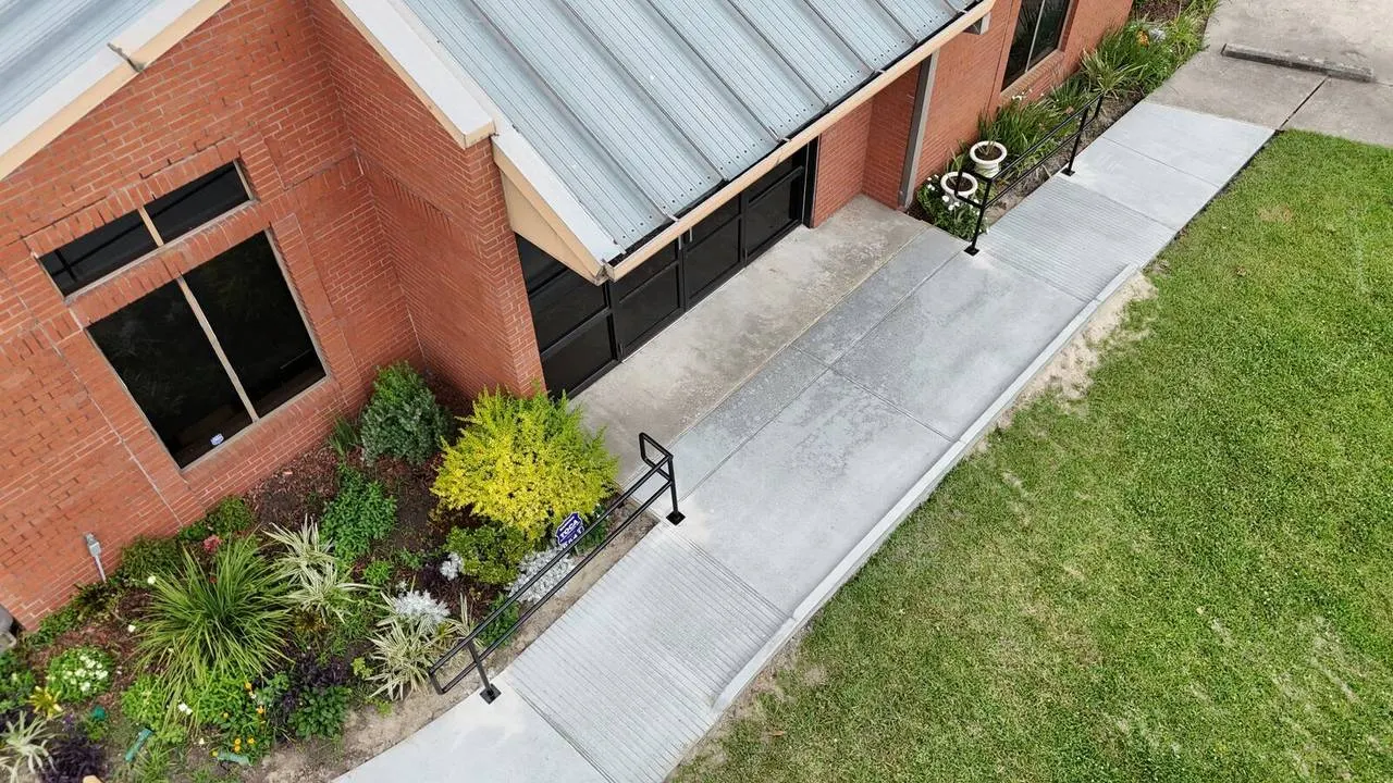 Oblique aerial view of completed curved ADA sidewalk with handrails and broom finished concrete at Jefferson Highway commercial facility in Jefferson Parish