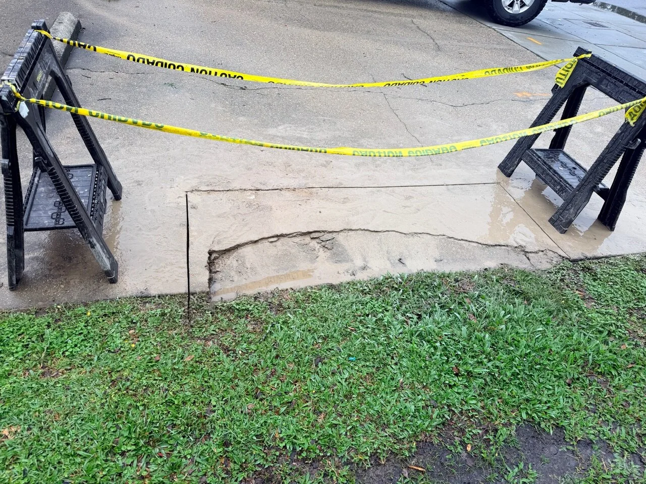 Caution-taped concrete sidewalk replacement work area with damaged slab fully removed on Jefferson Highway in Jefferson Parish Louisiana