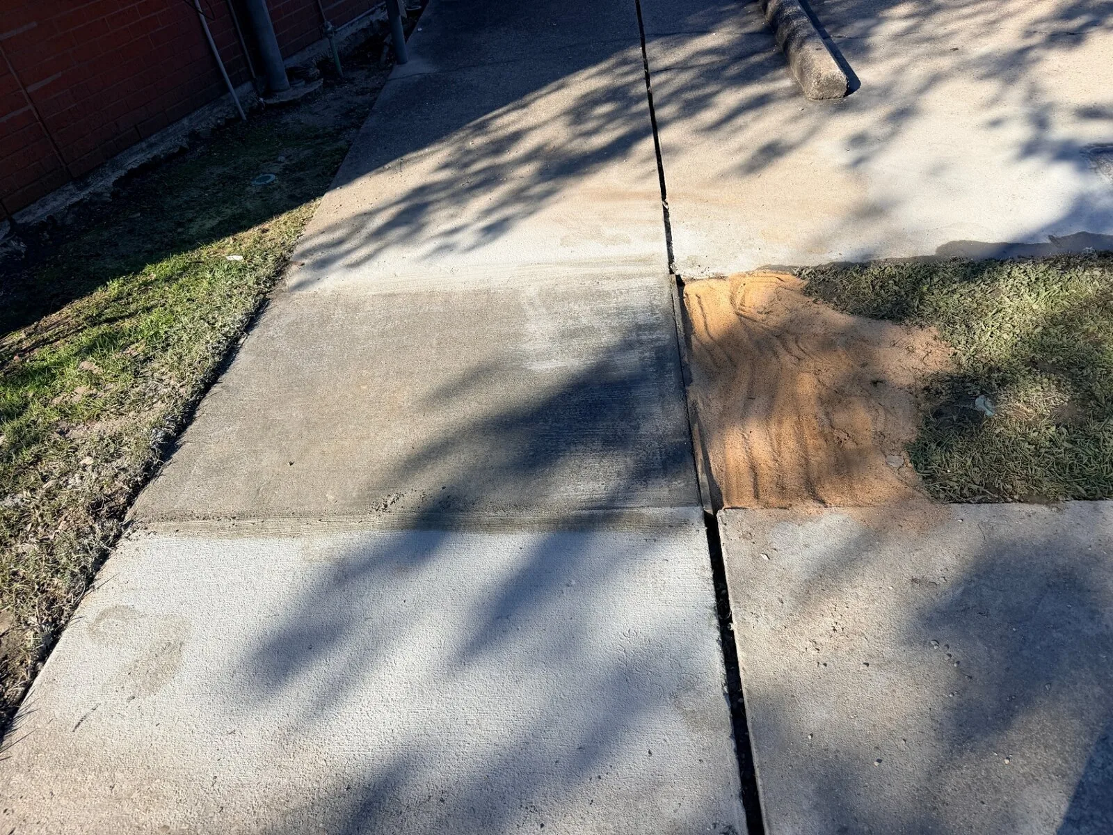 Completed second replacement sidewalk slab with sand-backfilled joints and matched elevation along brick building on Jefferson Highway in Jefferson Parish Louisiana