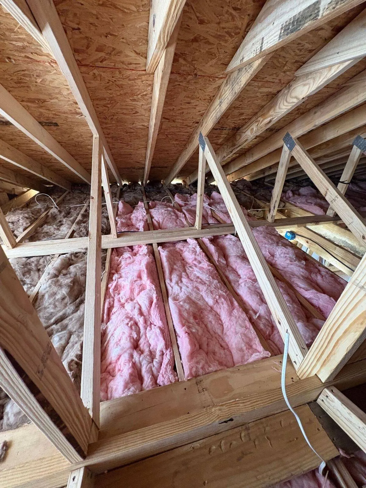 Attic insulation installation between roof trusses with fiberglass batt insulation in Gretna home