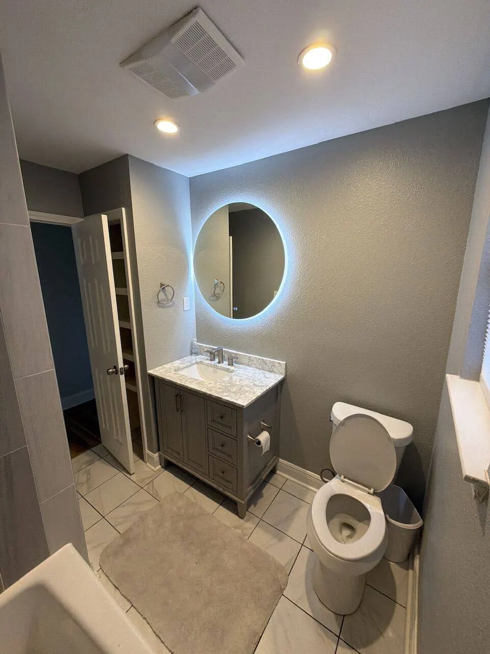 Finished bathroom with round LED backlit mirror and gray vanity in New Orleans