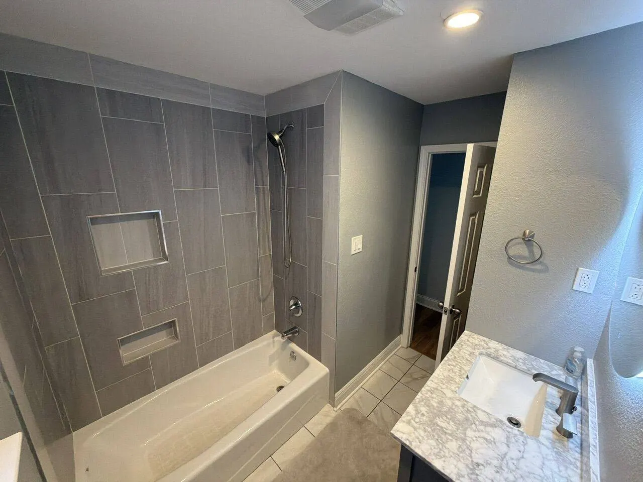 Completed bathroom with gray tile shower surround and marble vanity in Metairie Louisiana
