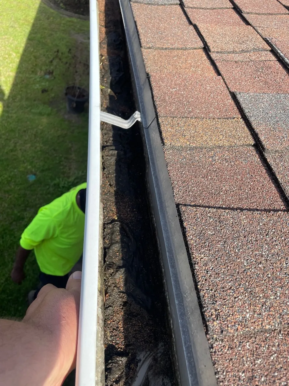 Cajun Home Services roofer inspecting a clogged gutter packed with shingle granules, asphalt debris, and sediment shed from the failing aged shingle roof on a Destrehan Louisiana home prior to re-roofing
