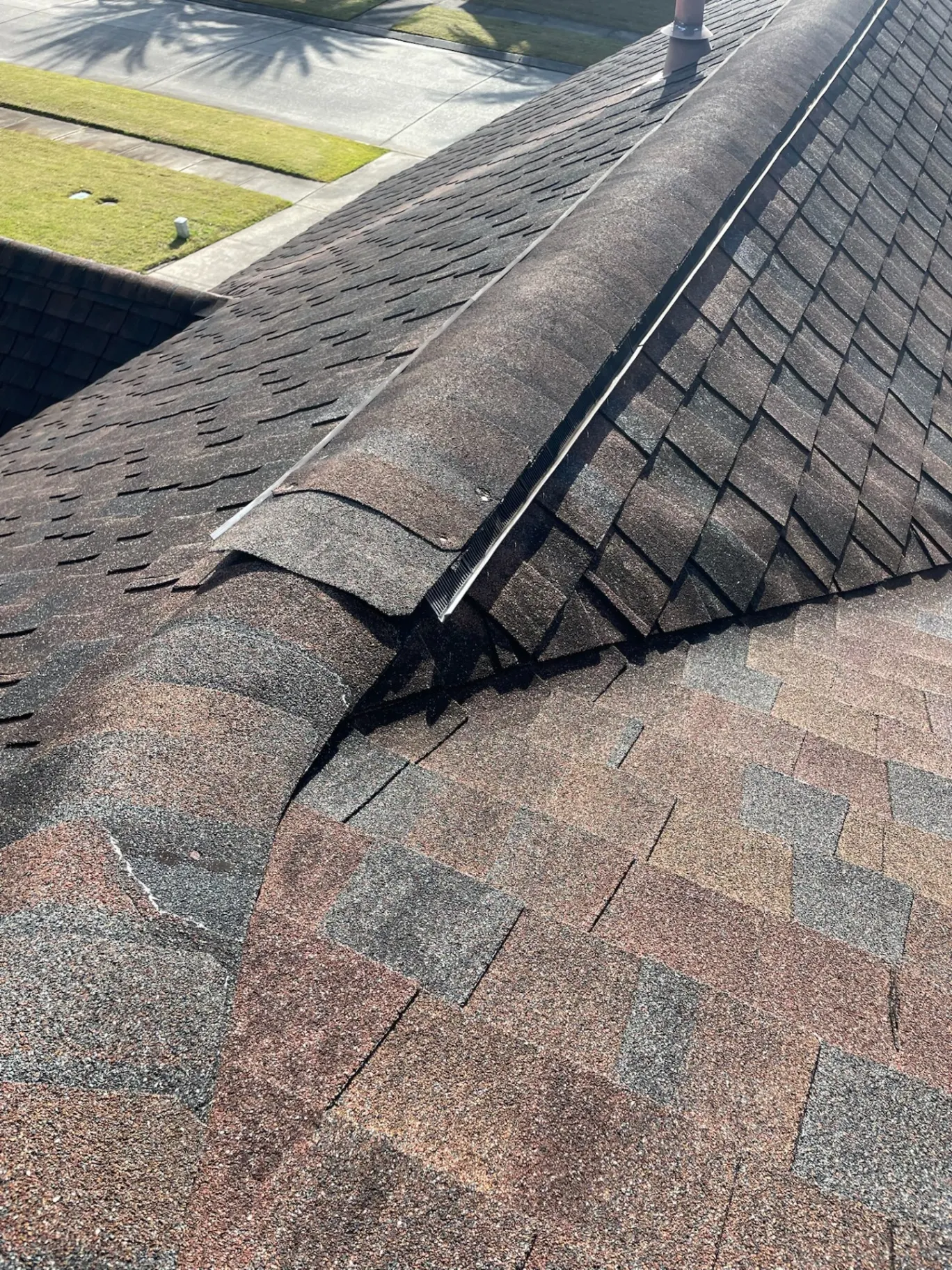 Close-up of buckling and displaced ridge cap shingles with exposed nails on a failing Destrehan Louisiana asphalt shingle roof prior to full replacement