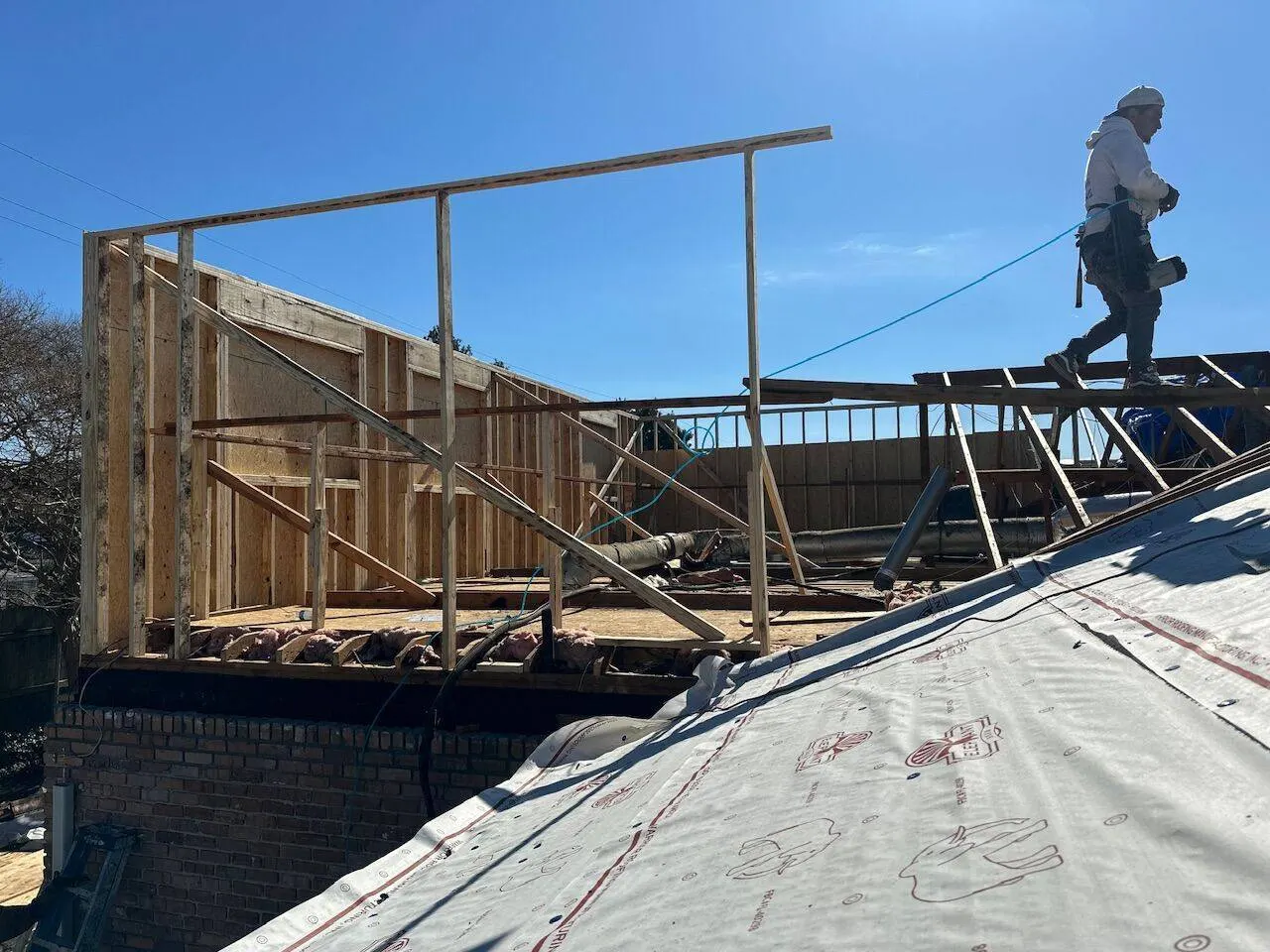 Crew member on roof walking framing during second story addition in Metairie