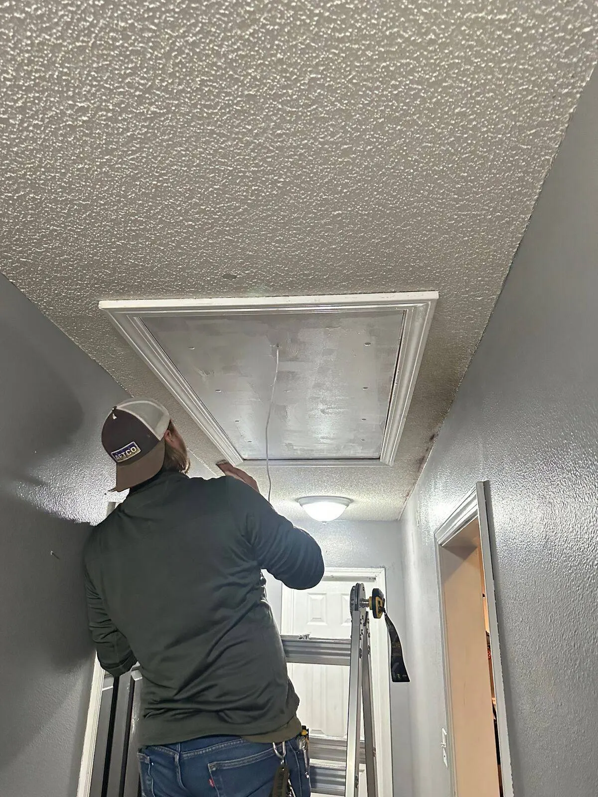 Technician installing attic ladder with trim work in Destrehan home hallway