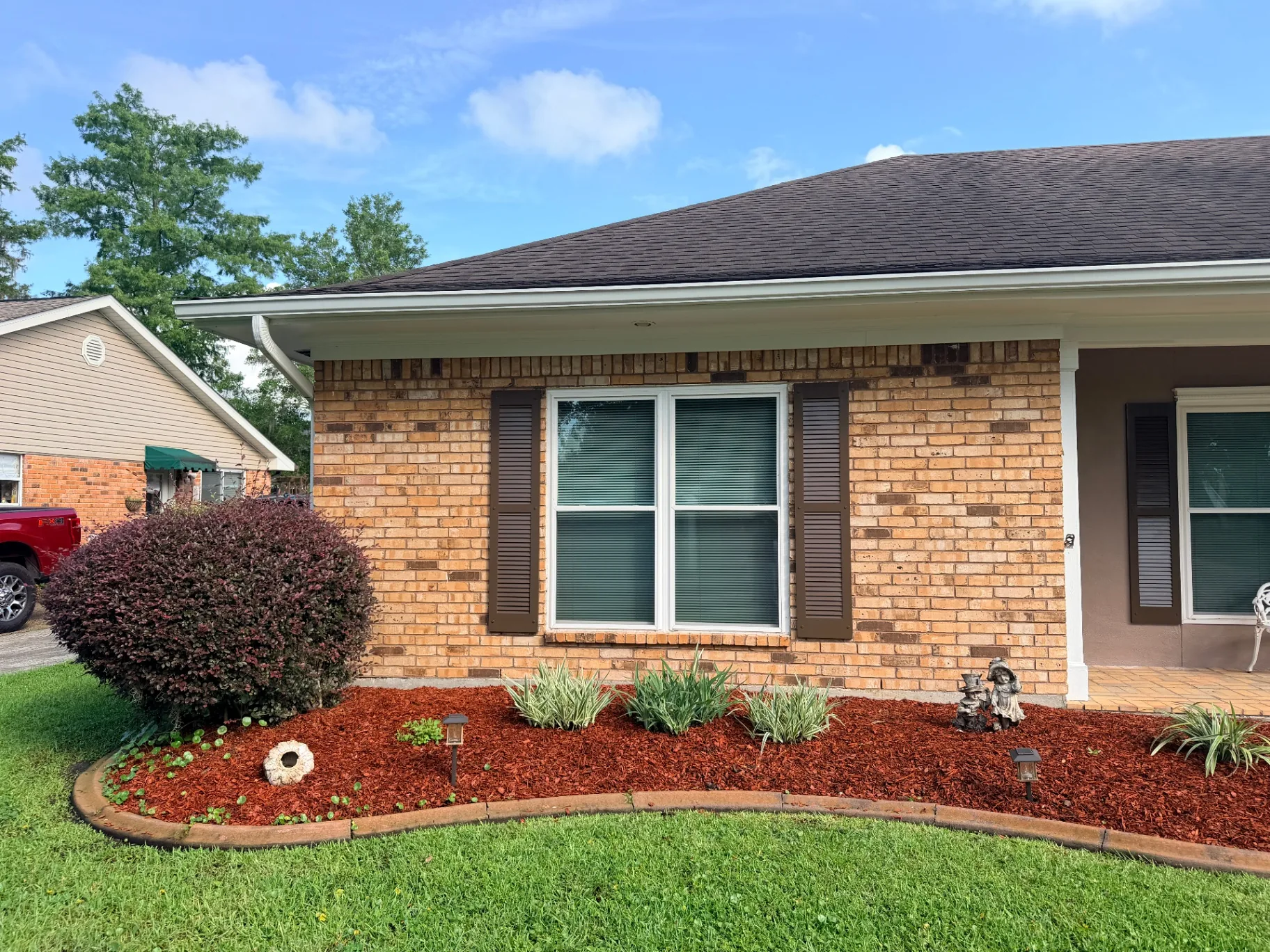 Newly installed brown louvered shutters on side window of Destrehan brick home