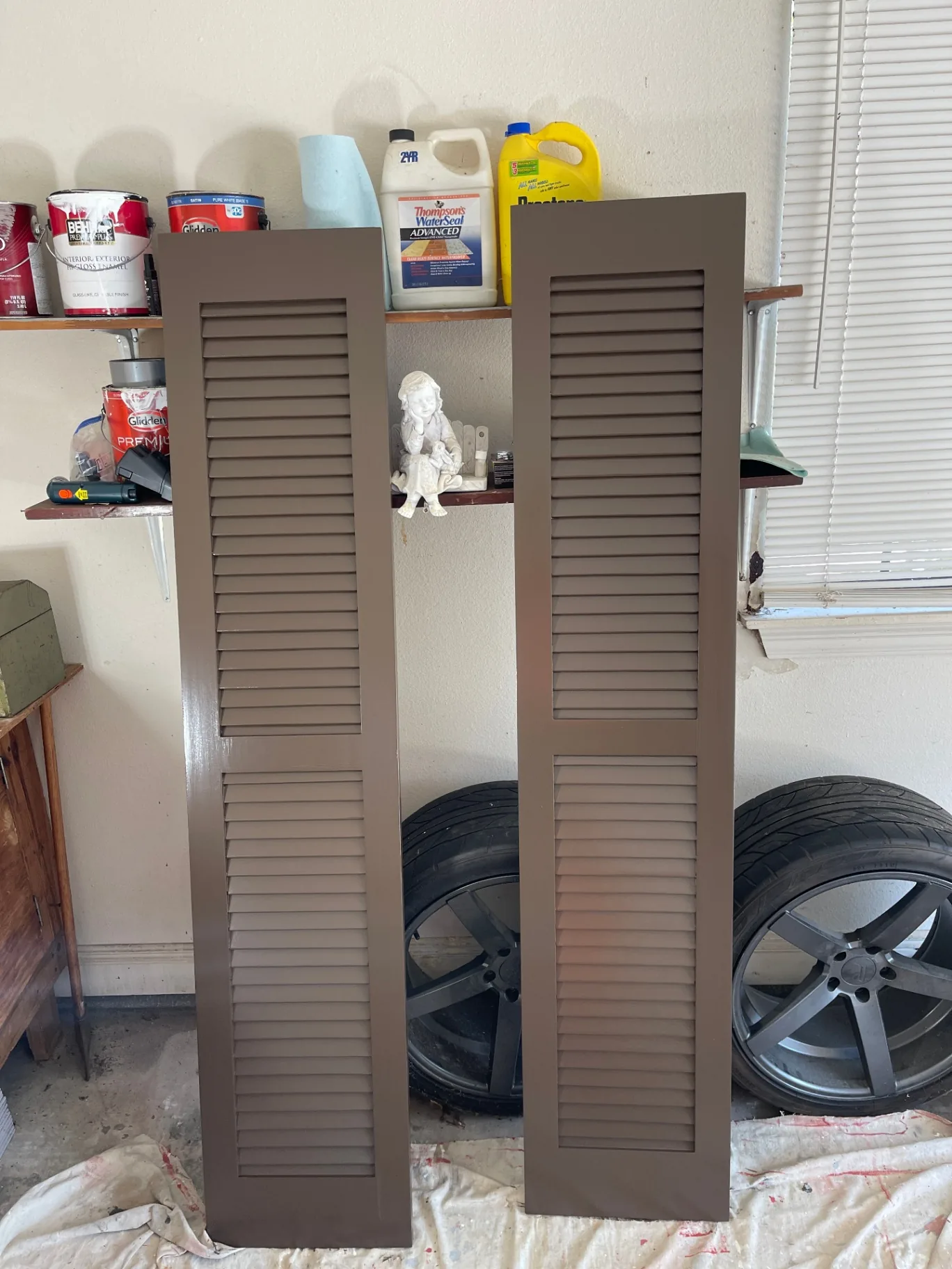 Two freshly hand-painted louvered shutters drying in garage for Destrehan shutter replacement project
