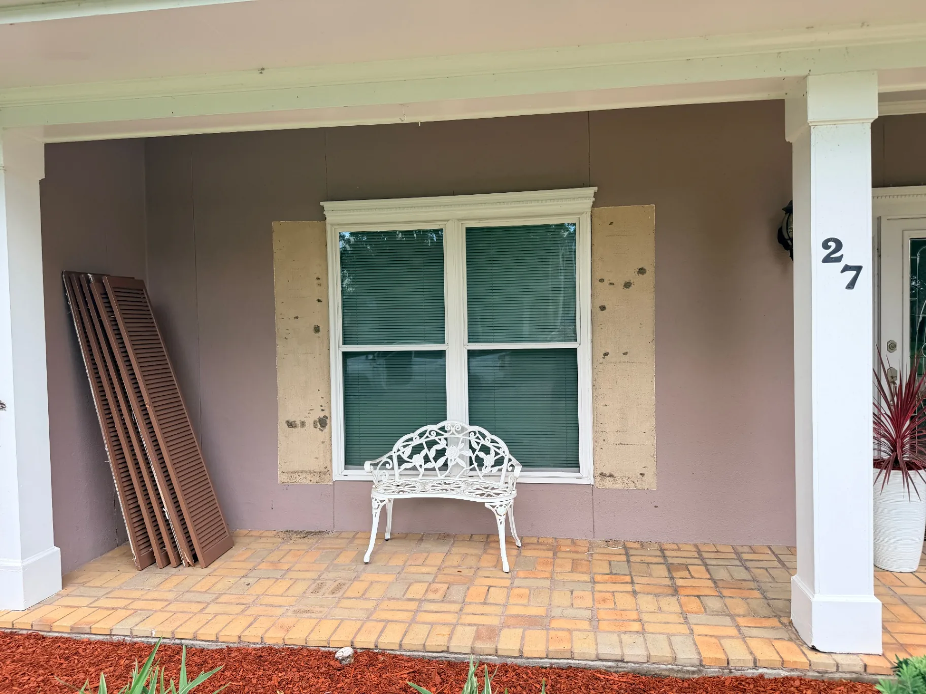 Front porch window with shutters removed and stack of old shutters ready for disposal in Destrehan