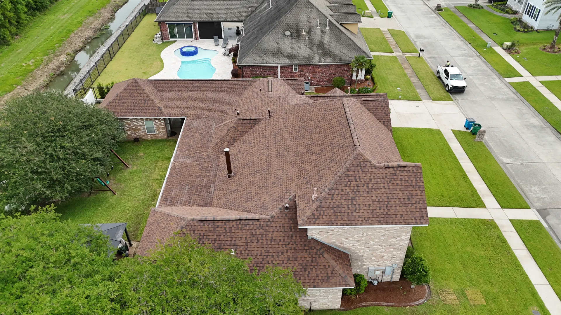 Aerial drone view of the completed multi-hip architectural shingle roof on a Destrehan Louisiana waterfront home with backyard pool, replaced by Cajun Home Services