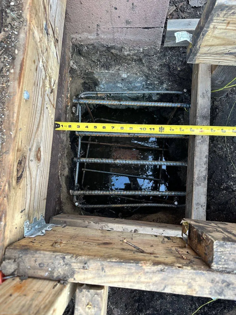 Rebar cage in foundation pier excavation with tape measure verifying depth in Metairie
