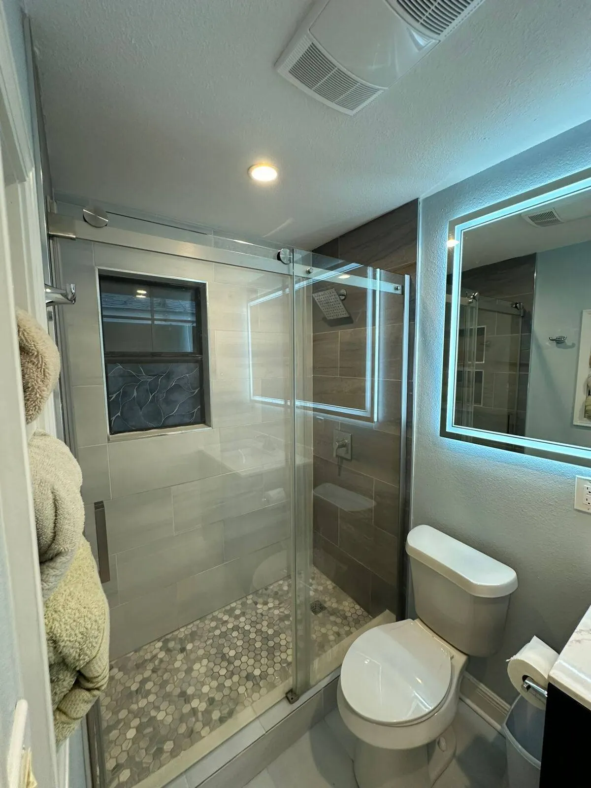 Frameless glass shower bathroom remodel with hexagon tile floor and LED mirror in Metairie LA