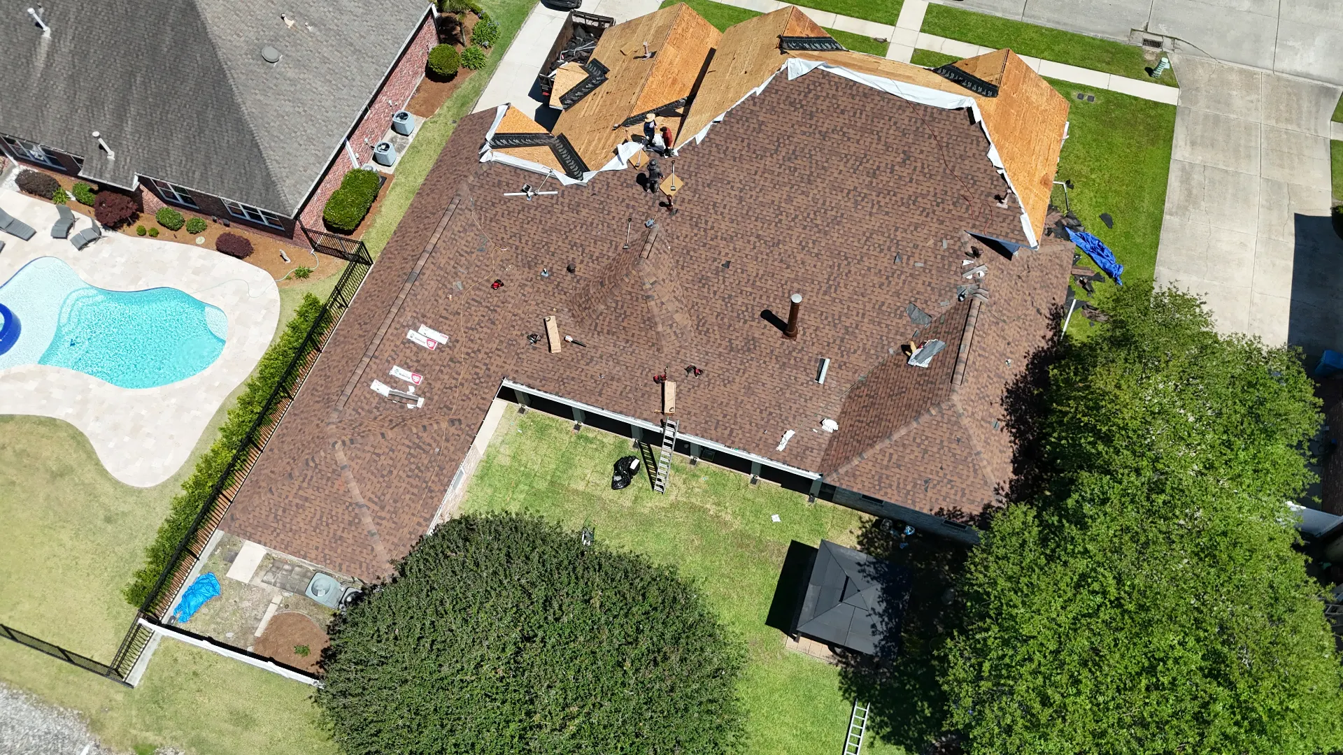 Aerial view of a Destrehan Louisiana home mid-roof-replacement showing one half completed with new architectural shingles and the other half opened to fresh decking, demonstrating Cajun Home Services' phased re-roofing strategy