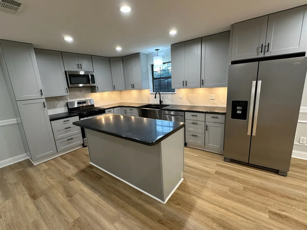 Completed kitchen remodel in Metairie Louisiana with light gray shaker cabinets, black quartz countertops, marble-look backsplash, stainless appliances, and LVP wood-look flooring by Cajun Home Services