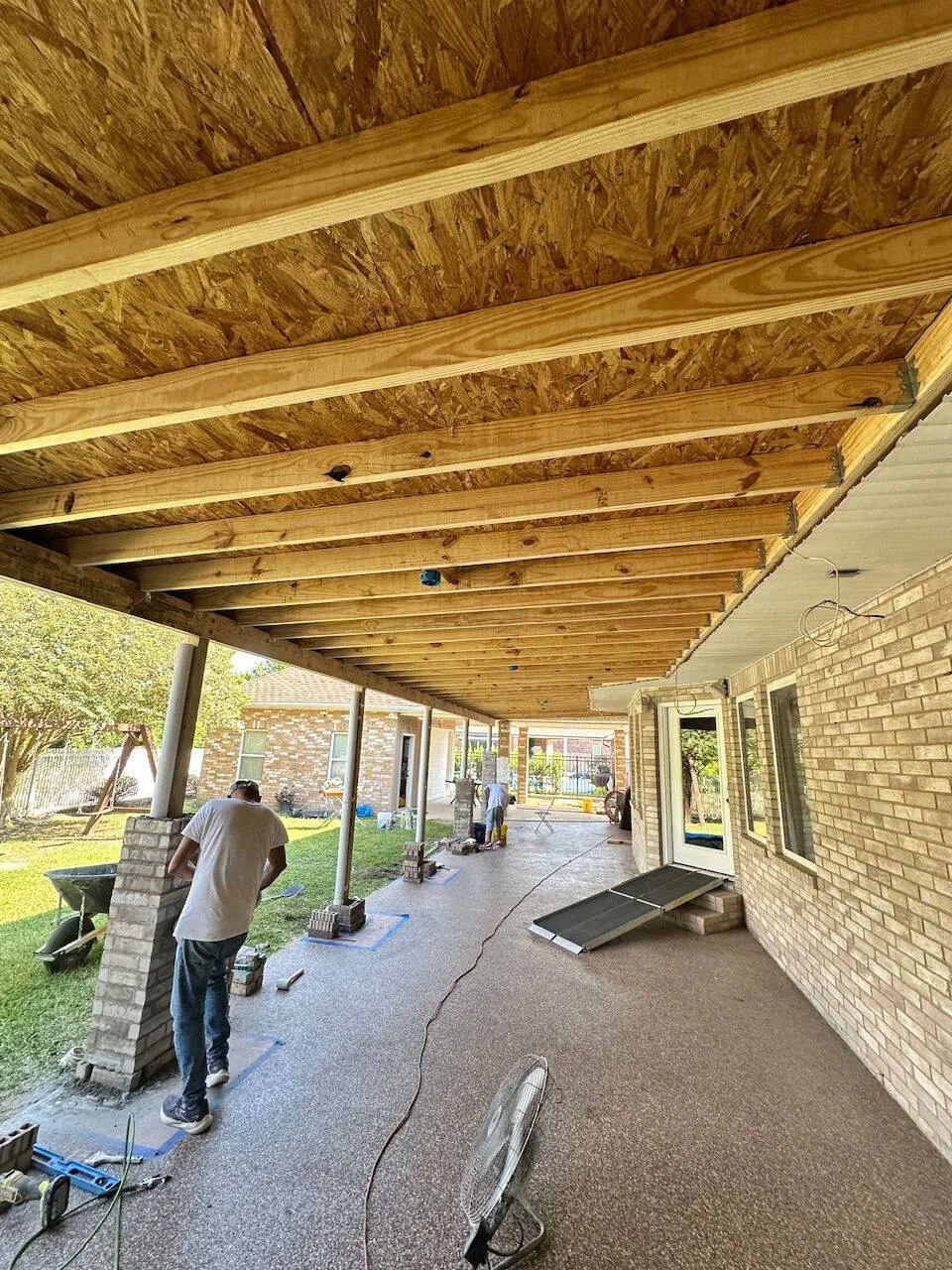 Covered patio underside showing OSB sheathing and beam framing with crew in Kenner LA
