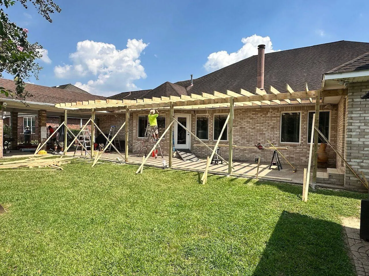 Crew framing large covered patio pergola with pressure-treated lumber on brick home in Kenner