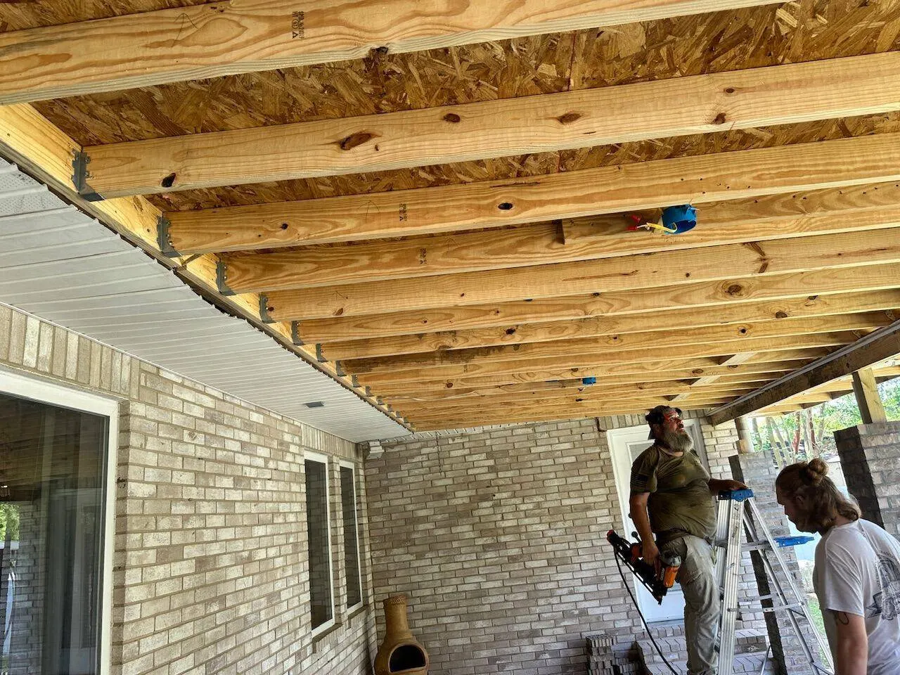 Crew installing soffit panels on covered patio with beam and joist framing in Kenner