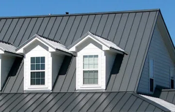 Standing seam metal roof on a home with white dormers and a clear blue sky