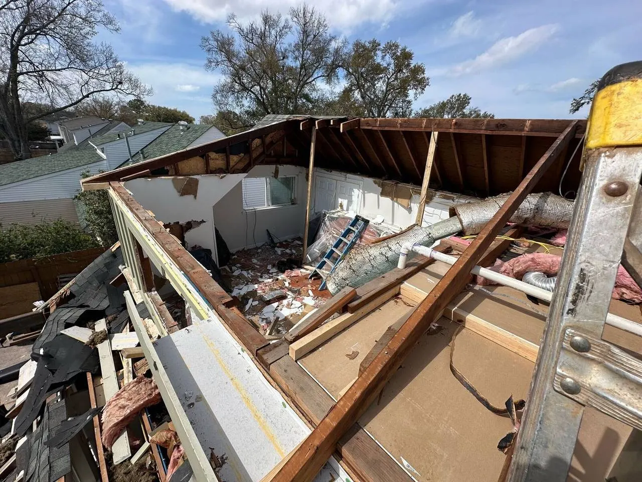 Storm damage roof tearoff showing exposed rafters and insulation removal in Metairie Louisiana