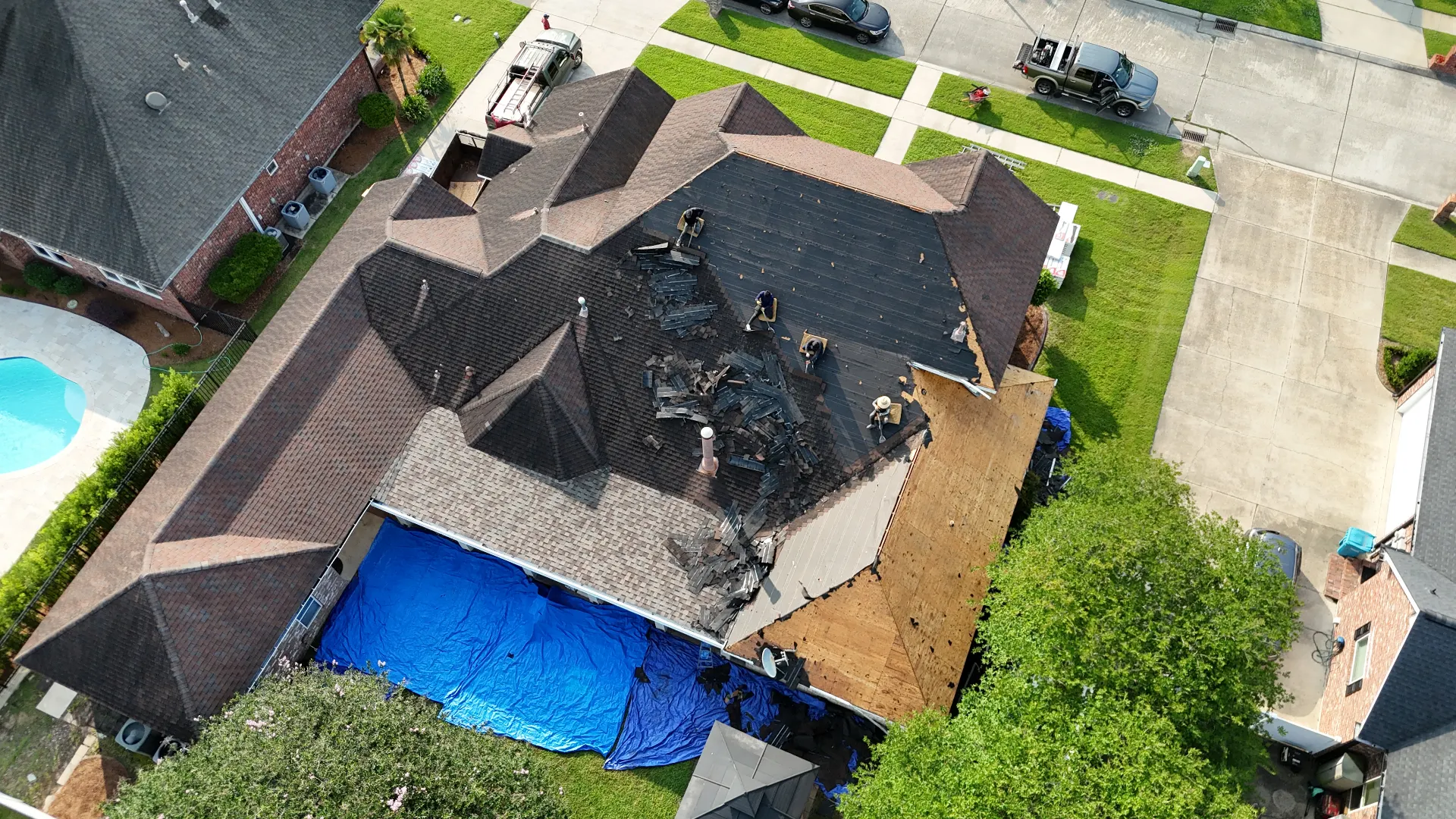 Aerial drone view of Cajun Home Services roofers performing a full shingle tear-off on a Destrehan Louisiana home, with old asphalt debris staged on the roof deck