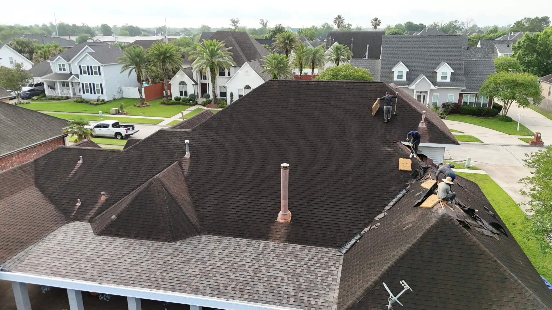 Cajun Home Services roofing crew tearing off aged architectural shingles section by section on a two-story Destrehan re-roof project